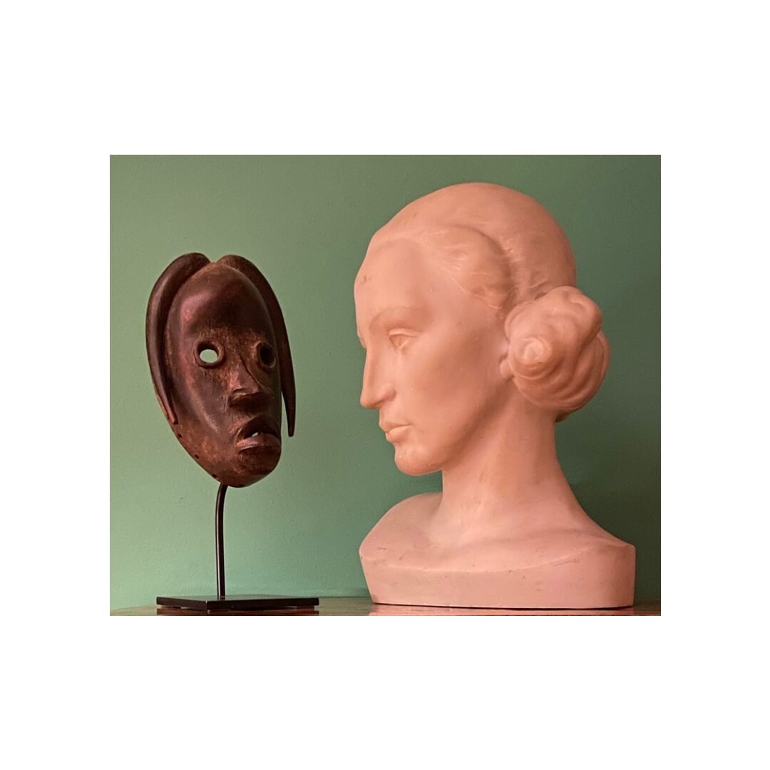 Maschera africana in legno accanto a un busto femminile in gesso su parete verde